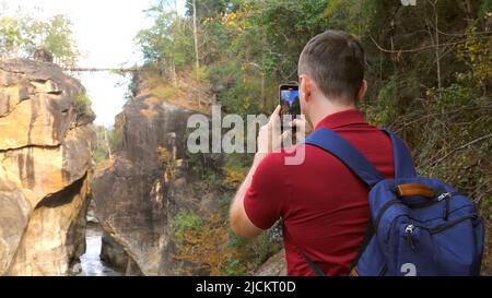 Casual travel blogger shooting video of amazing nature in national park in Thailand. Back view of 30s forest hiker photographer man with backpack make Stock Photo