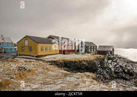 Flatey, Iceland, May 5, 2022: Houses on a cliff, painted in primary colors under a dark sky on which the sun breaks through Stock Photo