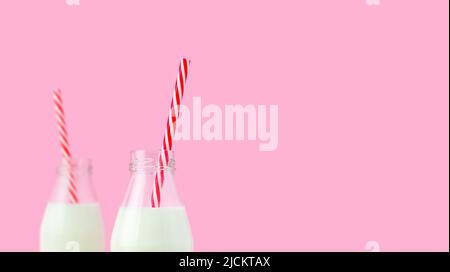 Fresh milk in a glass bottle, oatmeal, almond, alternative natural drink. Two bottles of healthy organic beverage with striped straws on a pink. Stock Photo