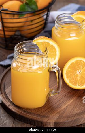 Two glasses of orange juice with orange sliceses on a wooden platter with basket of oranges in background Stock Photo
