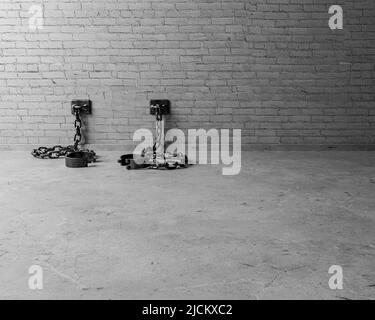 A set of empty old iron shackles draped on the floor connected to an isolated white brick wall  - 3D render Stock Photo