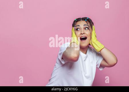Frightened woman yelling and closing her ears with her hands in yellow rubber gloves on pink background Stock Photo