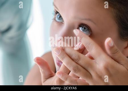 How to put contact lenses: Step by step photo instruction. Step 3: girl pulled back her lower eyelid and brought contact lens to her eye to put. Stock Photo