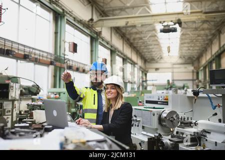 Male and female industrial engineers discussing factory's new machinery project and using laptop. Stock Photo