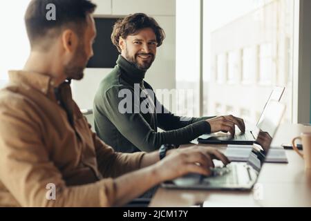 Cheerful colleagues using laptops and communicating, developing business project, discussing innovative ideas in office Stock Photo
