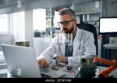 Robotics engineer working on desing of modern robotic arm aand sitting at desk in laboratory. Stock Photo