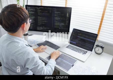 Software development concept, Male programmer typing data code and working on multiple screens. Stock Photo