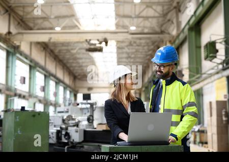 Male and female industrial engineers discussing factory's new machinery project and using laptop. Stock Photo