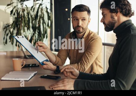 Partnership concept. Two serious businessmen studying documents, discussing business deal in office interior Stock Photo