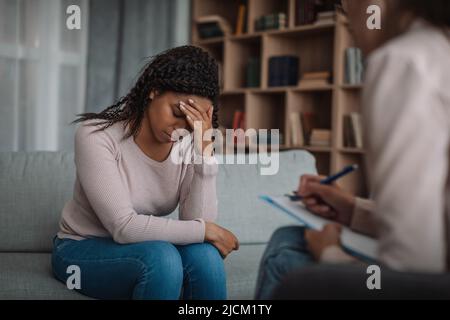 Sad unhappy black millennial woman crying on consultation with european psychologist in clinic Stock Photo