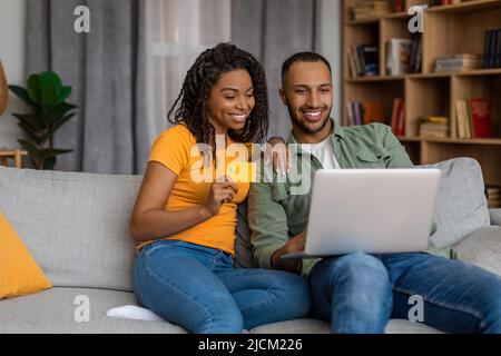 Online wallet and banking concept. Excited african american spouses using laptop and making purchases via internet store Stock Photo