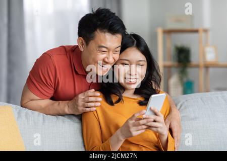 Happy asian lovers using smartphone, home interior Stock Photo