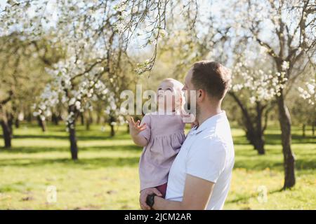 father and his adorable toddler daughter having fun in blossoming garden on beautiful spring day Stock Photo