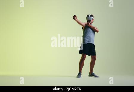 Mature man working out in virtual space. Athletic senior man playing a virtual fitness game using a pair of gaming controllers. Sporty senior man wear Stock Photo