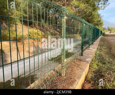 Green steel wire fence with rods near the irrigation canal Stock Photo