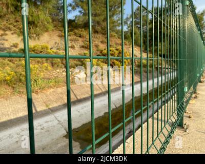 Green steel wire fence with rods near the irrigation canal Stock Photo