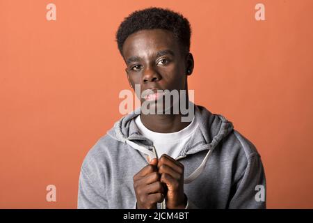 Isolated young African American male in hoodie looking at camera while joining hands and begging for something against brown background Stock Photo