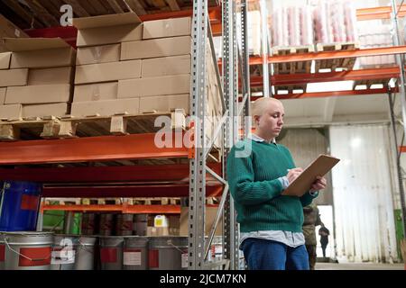 Female warehouse worker making notes in document to control number of goods on shelves during delivery Stock Photo