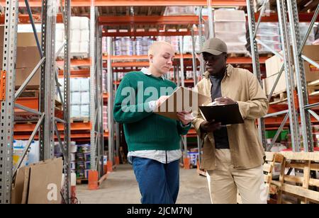 Multiethnic industrial workers checking their logistic lists while working with transportation of goods in warehouse Stock Photo