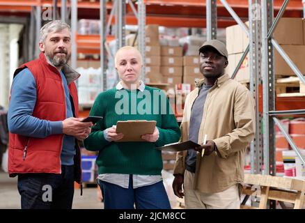 Portrait of group of multiethnic warehouse workers looking at camera while working with documents and tablet pc in storehouse Stock Photo