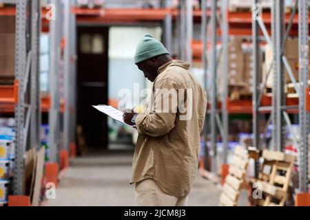 African American young supervisor making notes in document during his work in warehouse Stock Photo