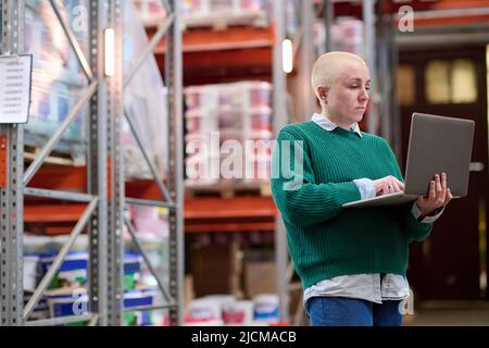 Young warehouse manager holding laptop and typing to check online delivery Stock Photo