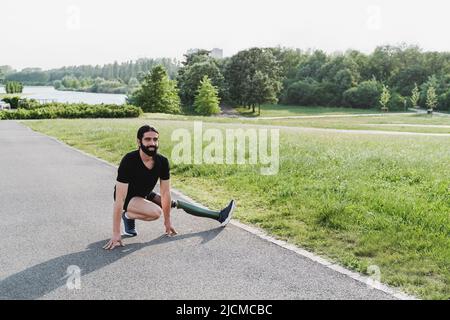 Fit man with disability doing warm-up stretching before exercise routine outdoor - Focus on face Stock Photo