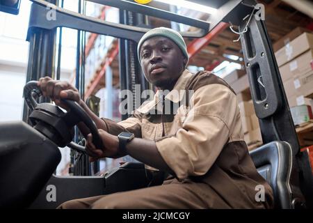 Portrait of African american driver looking at camera while driving forklift at warehouse Stock Photo