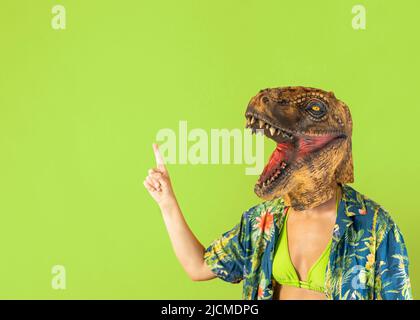 Woman in dinosaur animal mask showing advertisement, pointing at copy space for text. Business promo ad concept. Blank space isolated on green studio Stock Photo
