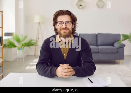 Portrait of happy businessman or teacher sitting at desk during online conference Stock Photo