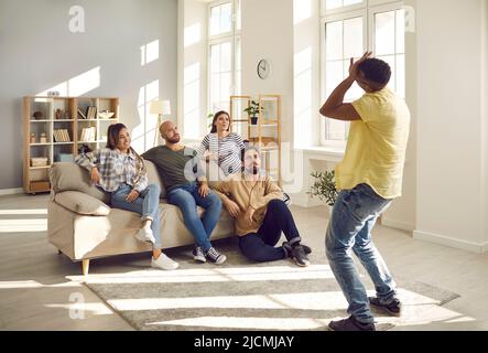Group of young cheerful friends have fun playing charades during casual gathering at home. Stock Photo