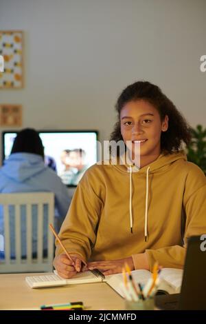 Smiling high school student doing homework when her sister ha Indian online class in background Stock Photo