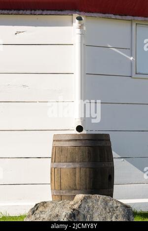 'Wooden barrel in front of a pipe, coming down from a white striped wall. ' Stock Photo