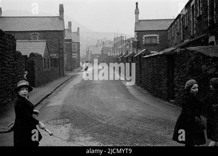 1950s, historical, a view up a damp side street in the welsh coalmining village of Trehafod, South Wales, with some school childern, one holding the handle of a skipping rope, playing outside. Stock Photo