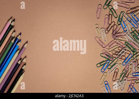 Colored pencils and stationery multi-colored paper clips on a brown background Stock Photo