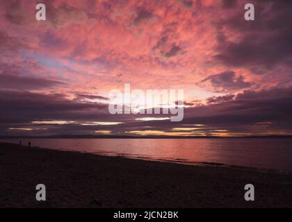 Pink & red colours of a fiery sunset afterglow on the clouds above the sandy Nairn central beach, & the Moray Firth. Stock Photo