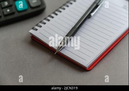 Calculator, pen, notepad lie on a gray surface. Open spring-loaded notebook with blank sheets. Close-up. Stock Photo