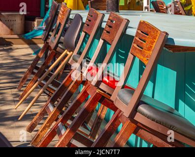 Tall wooden bar stools with backs stand in a row near the bar counter. Row of a tall chairs at the counter with beautiful natural sunlight. Outdoor fu Stock Photo