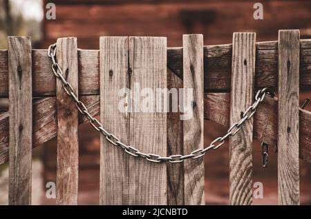 Old wooden gate closed with a rusty chain. Retro wood fence with vintage metal decorative elements. Rural background Stock Photo