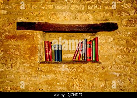 A shelf set in a brick wall with some very old books on Stock Photo
