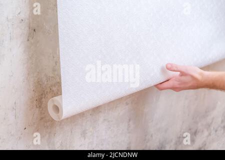 A man rolls out a roll of white wallpaper on the wall with glue. Wallpapering. Repair of a room, apartment, house. Stock Photo