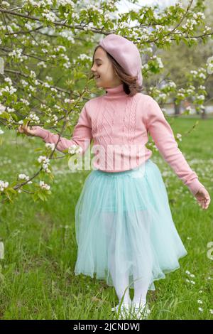 Adorable little girl stands next to a blooming white apple tree in the park. Stock Photo