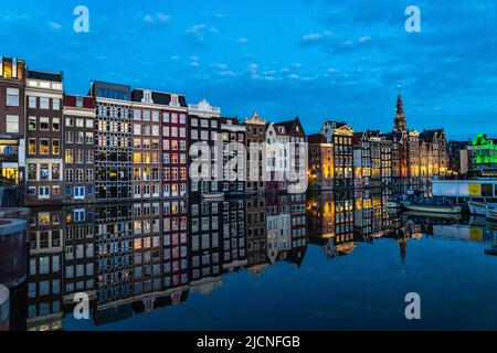 Canal houses on the Damrak, in the centre of the old town of Amsterdam, harbour, starting point of many canal tours, in the evening, church tower of t Stock Photo
