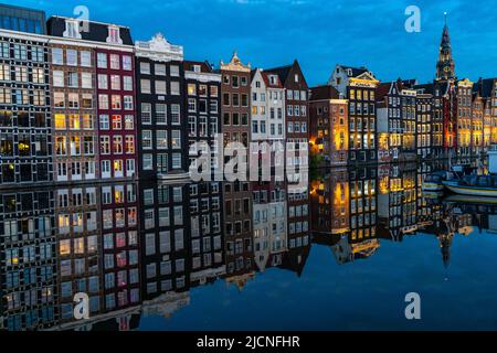 Canal houses on the Damrak, in the centre of the old town of Amsterdam, harbour, starting point of many canal tours, in the evening, church tower of t Stock Photo