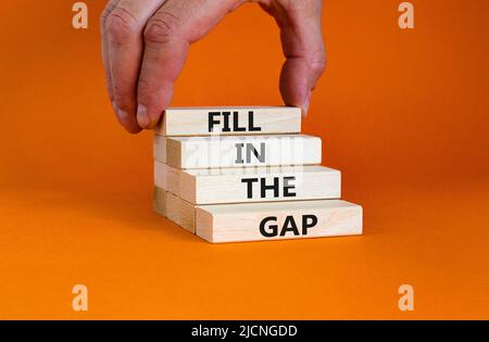 Fill in the gap symbol. Concept words Fill in the gap on wooden blocks on a beautiful orange table orange background. Businessman hand. Business, moti Stock Photo