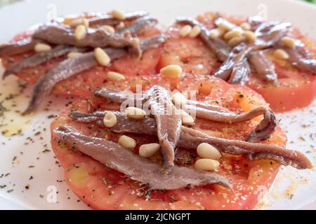 Close-up of organic tomato slices covered with anchovies and pine nuts Stock Photo