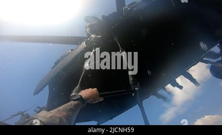 A Green Beret with 2nd Battalion, 10th Special Forces Group (Airborne), climbs a ladder fixed to a UH-60 Black Hawk helicopter near Key West, Florida, May 3, 2022. Helocasting, or free-drop from a helicopter, was conducted to familiarize Special Operations Forces personnel with insertion and extraction techniques in a waterborne environment often used in semi- or non-permissive areas. (DoD photo) Stock Photo