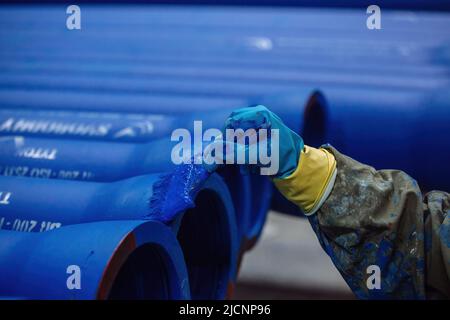 Worker painting new cast iron pipes in blue color. Stock Photo