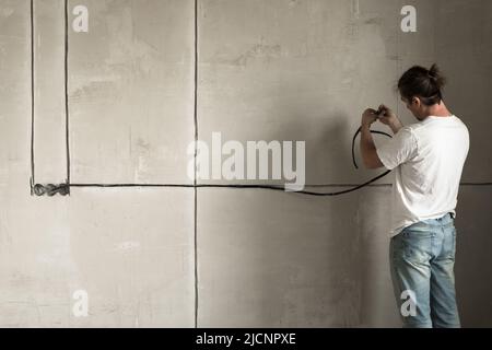 Renovation apartment. Electrical wiring. Empty walls, repairs house with their own hands. Man electrician installing laying electrical cables with Stock Photo