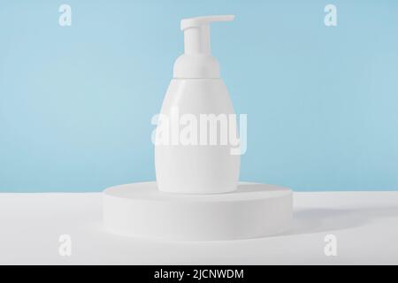 Bath soap white cosmetic bottle mockup on white podium pedestal on blue background. Body care foam product or lotion packaging. Plastic cosmetics tube Stock Photo